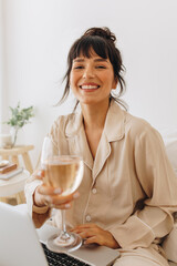 Smiling woman holding wine glass while working on laptop