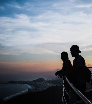 Silhouette of backpacking tourist couple watching the sunset over Copacabana Beach in the city of Rio de Janeiro, Brazil, from the top of Sugarloaf Mountain aka Pão de Açúcar