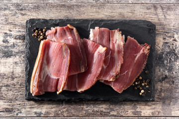 Dried and smoked meat slices on wooden table