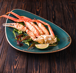 Crab legs with fresh lemon slices in a green plate on a dark wooden background. Restaurant. Ready to eat.