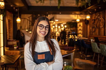 Portrait of a beautiful waitress wearing an apron, smiling at camera. Portrait of positive young woman working professional confectioner in own coffee shop, looking at camera with toothy smile.
