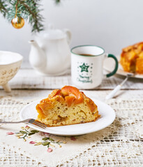 A slice of fruit pound cake, tea mug, Christmas tree branch on white wooden background, closeup view