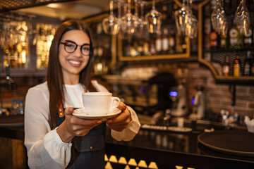 Female Barista serving cup of fresh coffee for you. Shot of a young barista serving a cup of coffee to a customer. Attractive waitress serving coffee at cafe