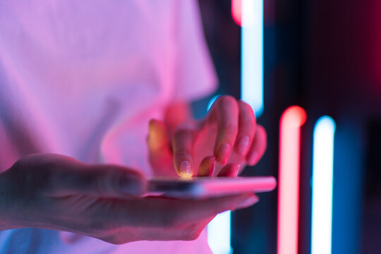 Mobile phone in the light of neon in women's hand. A person writes a message in a chat on the colored background