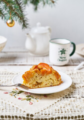 A slice of fruit pound cake, tea mug, Christmas tree branch on white wooden background
