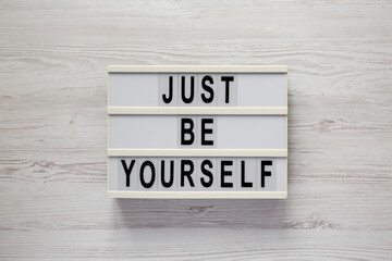 'Just be yourself' on a lightbox on a white wooden background, top view. Flat lay, overhead, from above.