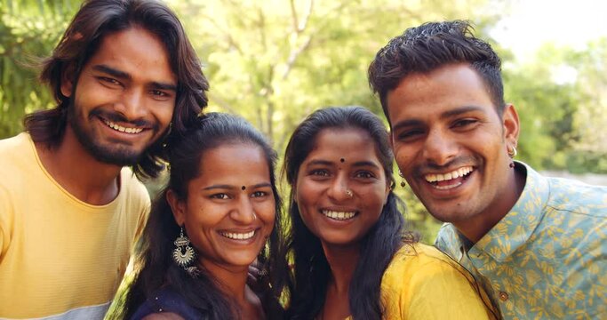 Four friends, two female sand two males, stand pose together under tree in nature park garden lawn for a camera selfie photo video pose with toothy smile and say cheese laugh