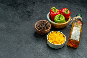 side view of bowl of bell peppers on the right side with herb and vegetable bowls oil bottle on side on green table