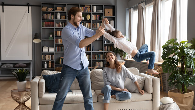 Wide banner view of loving young Caucasian father have fun play with excited small daughter relax at home. Caring parents feel playful engaged in funny activity with little girl child in living room.