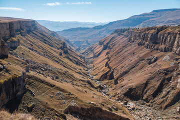 Narrow curving river runs between high hills bare slopes in picturesque deep canyon against mountains under clear blue sky on sunny day