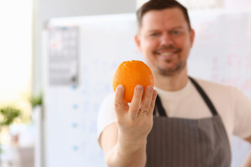 Smiling Chef Vlogger Holding Orange Ingredient. Man Cooking from Fruit in Kitchen at Home. Preparing Fresh Citrus Vegetarian Food. Culinary Recipe from Person Standing in Apron. Partial View Shot