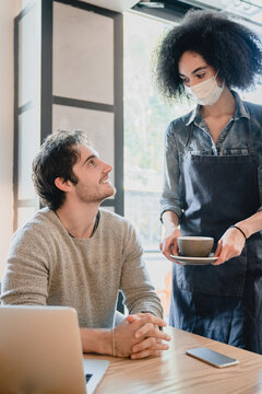 Vertical Shot Of Black Waitress In Medical Mask Against Covid 19 Servicing Customer With Laptop