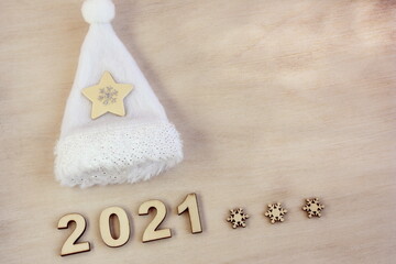 New year number 2021 lined with wooden figures on the wooden surface next to the white Christmas hat. Happy New Year.
