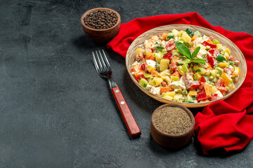 side close view of veggie salad on red napkin with fork notepad and pepper on side and free place for text on dark grey background