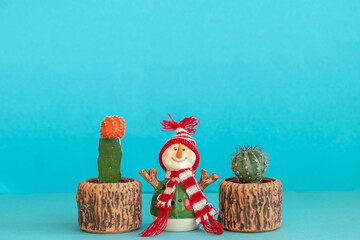 A snowman stands between two different cacti on a blue background. Merry Christmas and happy new year concept.