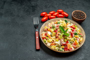 side close view of bowl of veggie salad with fork tomatoes pepper on side and free place for text on dark grey table