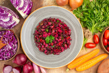 top view healthy salad on a ceramic plate with fresh vegetables nearby such as a red cabbage parsley bunch bowl of roma tomatoes carrot potatoes and onions on a wooden table