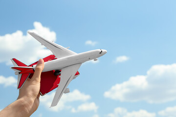 Woman holding toy airplane and passport against blue sky, closeup
