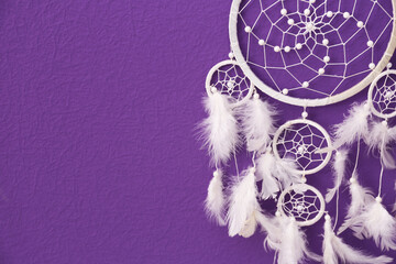 Beautiful handmade dream catcher on purple wall, closeup. Space for text