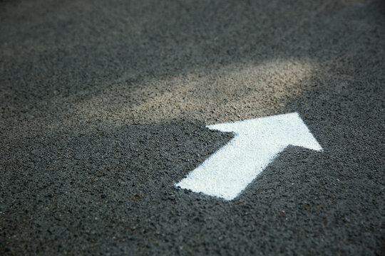 White arrow painted on asphalt. Space for text