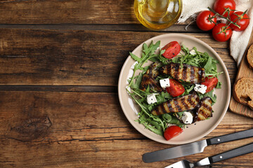 Delicious salad with roasted eggplant, feta cheese and arugula served on wooden table, flat lay. Space for text