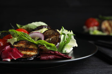 Delicious salad with roasted eggplant and basil served on black wooden table, closeup