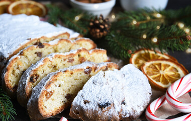 Sliced homemade Christmas dessert stollen with raisins and nuts on  rustic table with cinnamon. Christmas tree branches, selective focus