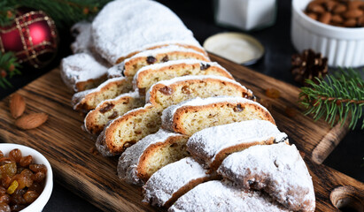 Sliced homemade Christmas dessert stollen with raisins and nuts on  rustic table with cinnamon. Christmas tree branches, selective focus
