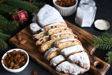 Sliced homemade Christmas dessert stollen with raisins and nuts on  rustic table with cinnamon. Christmas tree branches, selective focus