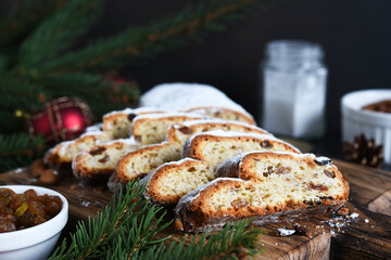 Sliced homemade Christmas dessert stollen with raisins and nuts on  rustic table with cinnamon. Christmas tree branches, selective focus