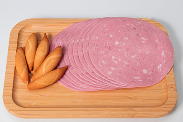 Slices of mortadella accompanied by slices of bread on a wooden board with a white background and a very bright base