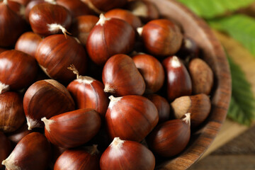Fresh sweet edible chestnuts in wooden bowl, closeup