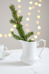 Obraz na płótnie Canvas Minimalistic Christmas decoration. A branch of fir tree in a white vintage pitcher and fairy lights in the background