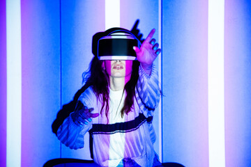Woman using virtual reality headset, moving hand at interactive technology exhibition with multicolor projector light illumination, immersive concept