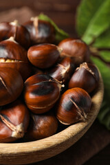 Delicious roasted edible chestnuts in wooden bowl on table, closeup