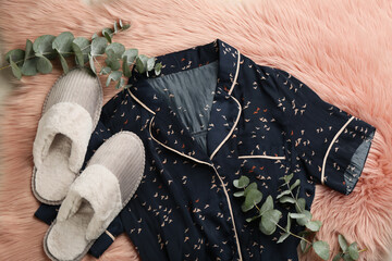 Pair of fluffy slippers, pajamas and eucalyptus branches on fuzzy carpet, flat lay. Comfortable...