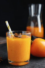 Tasty persimmon smoothie with anise and straw on black table