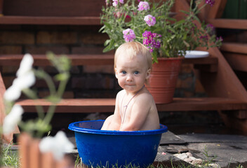 a little girl is sitting in a blue basin of water on the street near the house, bathing and something is very surprised
