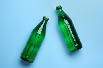 Glass bottles with water on light blue background, flat lay