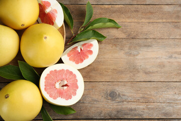 Fresh cut and whole pomelo fruits on wooden table, flat lay. Space for text