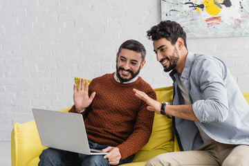 Smiling hispanic father and son having video call on laptop at home, two generations of men