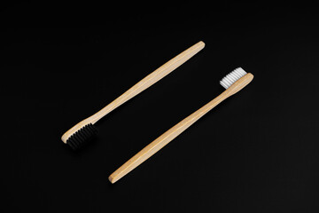 Two Eco-friendly antibacterial bamboo wood toothbrushes with white and black bristles on a black background. Taking care of the environment is trending. Tolerance. Copy space