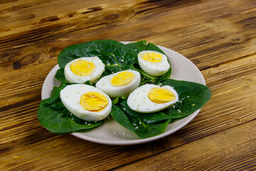 Boiled eggs with fresh spinach leaves and sesame seeds on wooden table