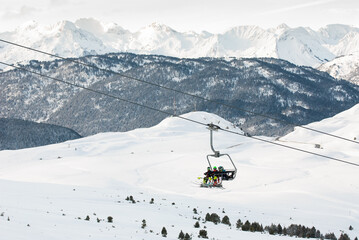 Paisaje invernal de alta montaña con esquiadores montados en telesilla.
