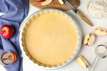 Baking dish with dough for traditional English apple pie and ingredients on white table, flat lay