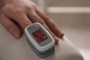 Man measuring oxygen level with modern fingertip pulse oximeter indoors, closeup. Space for text