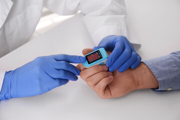 Doctor checking patient's oxygen level with pulse oximeter at light grey table, closeup