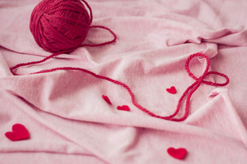 Woolen yarn and red felt hearts on a pink textile background. Love concept, holiday concept, Valentine's day, 14 February.