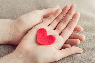 Heart in human hands. Red heart made of felt in the palm of a person. Holiday concept, health concept. February 14, Valentine's Day