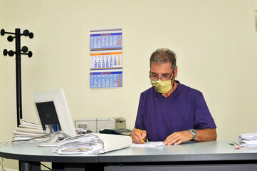 A man wearing a face mask while at work sitting at a desk. 